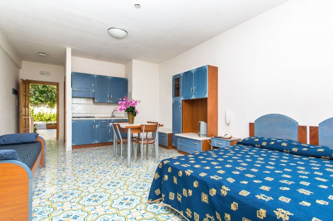 Monolocale con letto, cucina blu e tavolo.