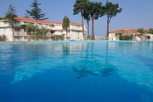 Piscina con acqua limpida, vari edifici e alberi sullo sfondo.