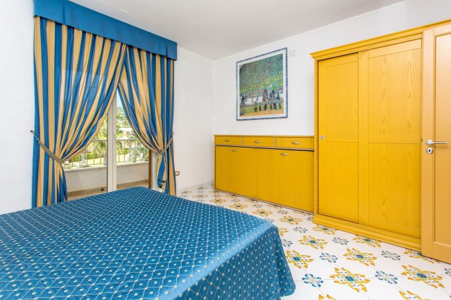 Camera con letto blu, armadio giallo, tende coordinate e pavimento decorato.