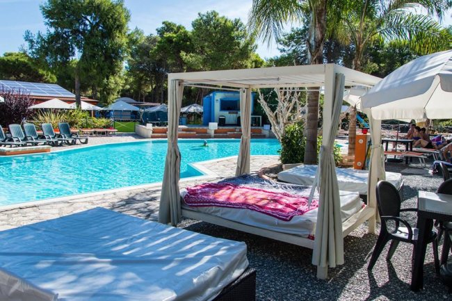 Una piscina con lettini, gazebo con tende bianche e un'atmosfera rilassante.