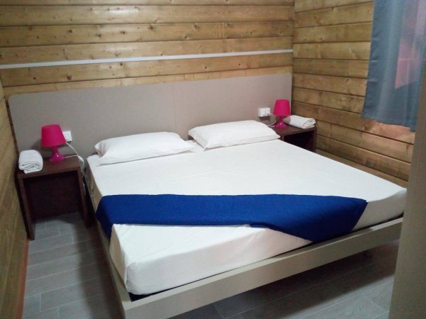 Camera da letto con letto matrimoniale, due comodini e lampade rosa.