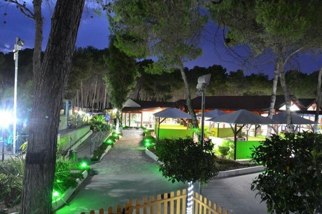 Giardino di sera con vialetti illuminati, alberi e gazebi.