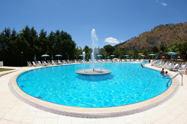 Piscina con fontana centrale e sdraio.