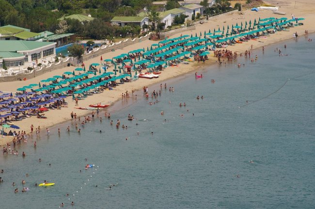Spiaggia affollata con ombrelloni verdi e azzurri.