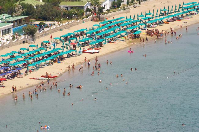 Spiaggia affollata con ombrelloni turchesi e bagnanti in mare.