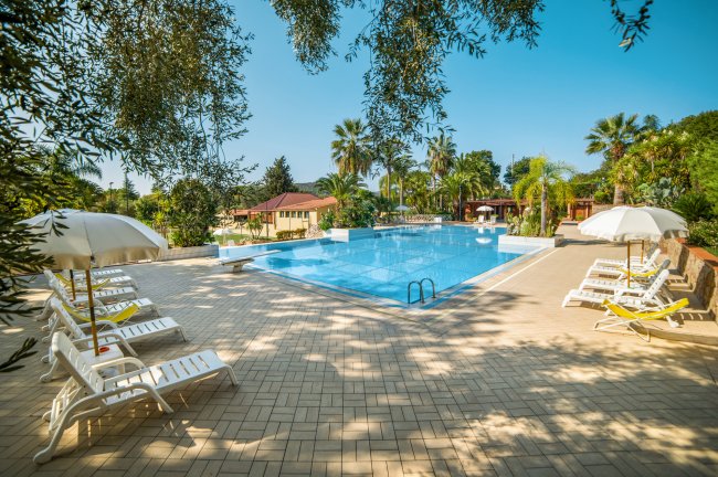 Piscina all'aperto con lettini e ombrelloni bianchi, circondata da palme.