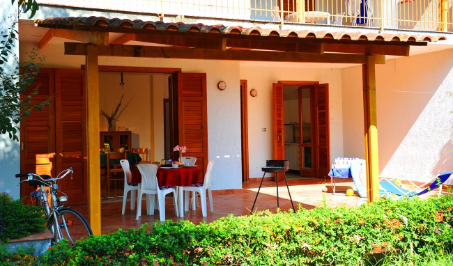 Una veranda esterna con tavolo apparecchiato, sedie bianche, barbecue e bicicletta.