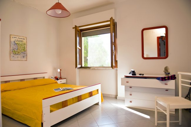 Una stanza con letto matrimoniale giallo, finestra aperta e comò bianco con specchio.