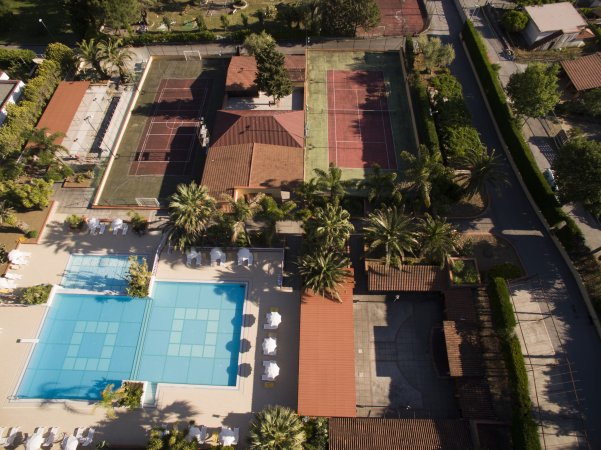 Vista aerea di un resort con piscine, campi da tennis e palme.