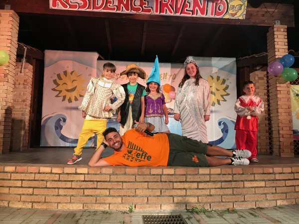 Bambini in costume su un palco con un adulto sdraiato davanti.