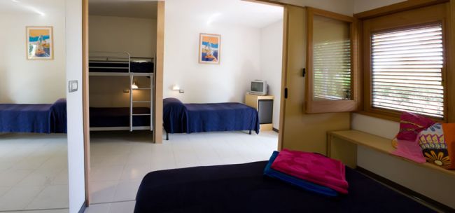 Una stanza con letto a castello, letto singolo, piccolo televisore e asciugamani colorati.