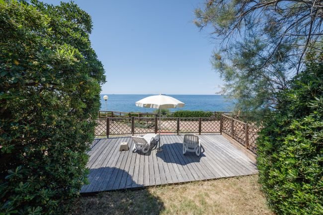 Terrazza con sedie e vista mare, incorniciata da arbusti.