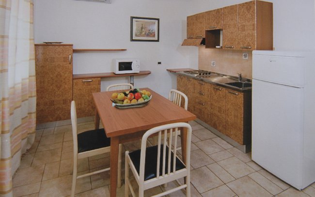 Cucina con tavolo da pranzo, quattro sedie, elettrodomestici e cestino di frutta.