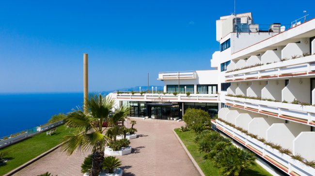 Edificio moderno di un hotel, vista sul mare con palme e cielo blu.