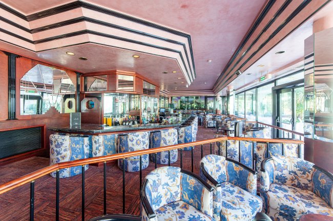 Interno di un bar elegante con sedie fiorite e grandi finestre.