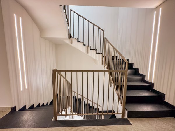 Scala moderna con ringhiere in metallo e luci a LED lungo le pareti.