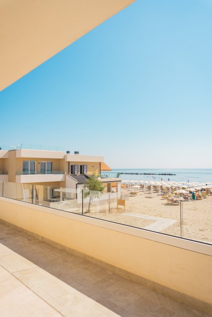 Vista da un balcone su una spiaggia con lettini e un edificio moderno.