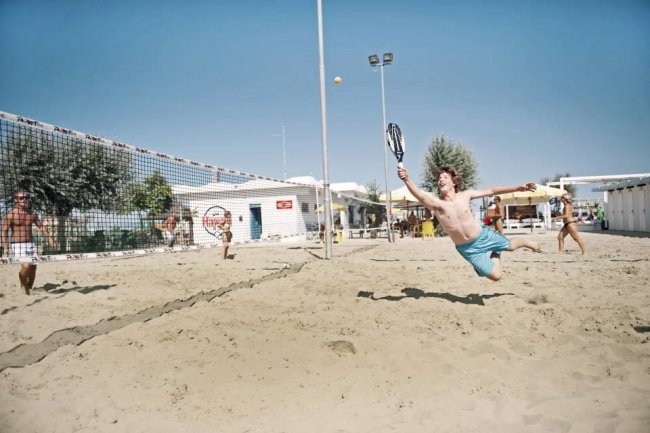 Persone giocano a beach tennis sulla sabbia, attorno a una rete.