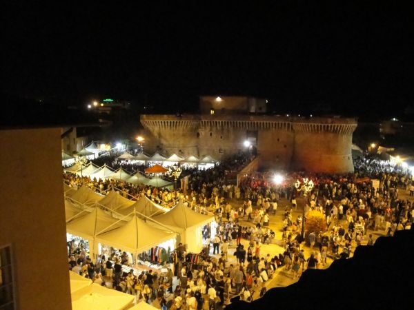 Vista notturna di una fortezza circondata da una folla e tendoni bianchi illuminati.