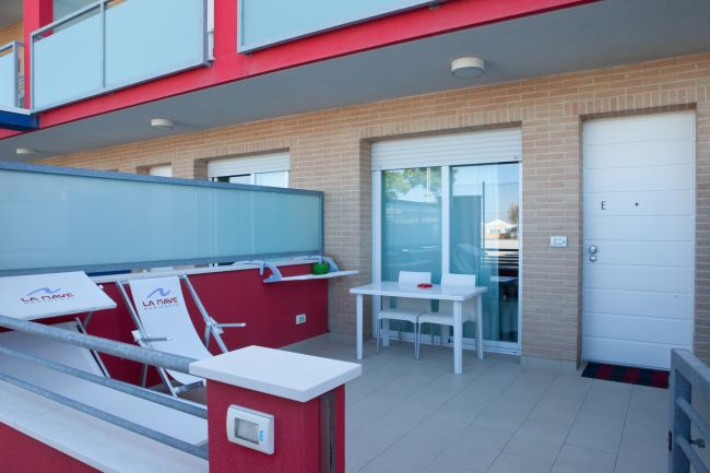 Terrazza con sedie a sdraio e tavolino bianco davanti a un appartamento.