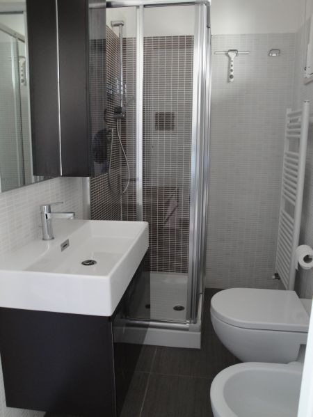 Bagno moderno con doccia, lavabo bianco e WC in una piccola cabina.