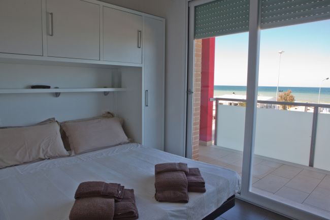 Camera con letto matrimoniale, asciugamani piegati e vista mare dalla finestra.