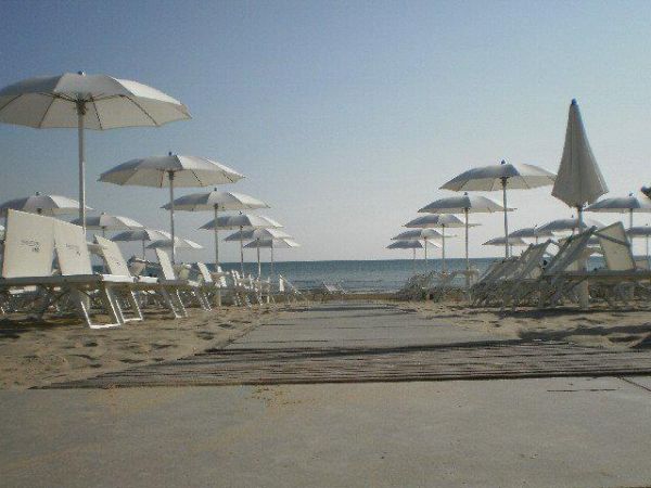 Ombrelloni e lettini bianchi su una spiaggia sabbiosa con il mare sullo sfondo.