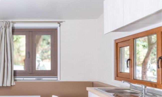 Interno di una cucina con finestre marroni, mobile bianco e lavello in acciaio.