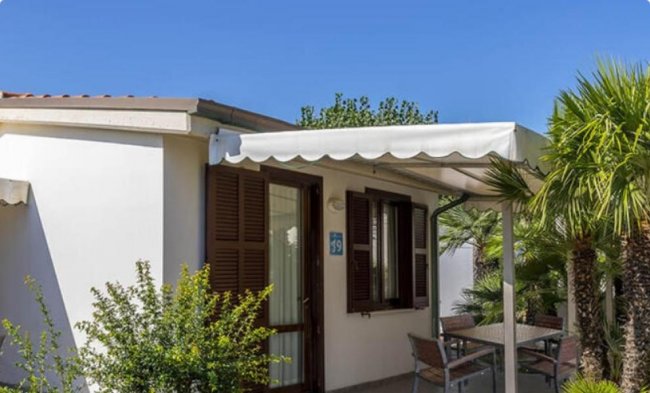 Esterno di una casa con veranda, sedie, piante e cielo sereno.