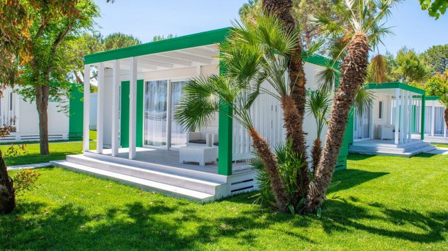 Una villetta bianca e verde con veranda, circondata da erba e alberi tropicali.