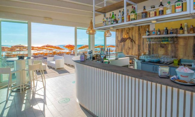 Un bar moderno con vista sulla spiaggia, ombrelloni arancioni fuori.