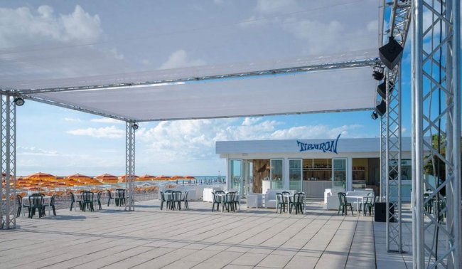 Un'ampia terrazza con sedie e tavoli bianchi e neri, ombrelloni arancioni sullo sfondo.