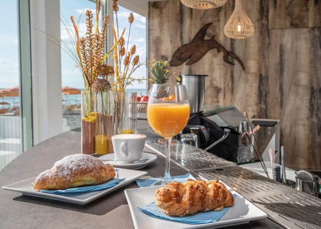 Colazione con croissant, succo d'arancia e caffè su un bancone vicino alla spiaggia.