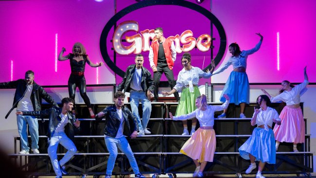 Gruppo di persone in abiti anni '50 che ballano su un palco con l'insegna 