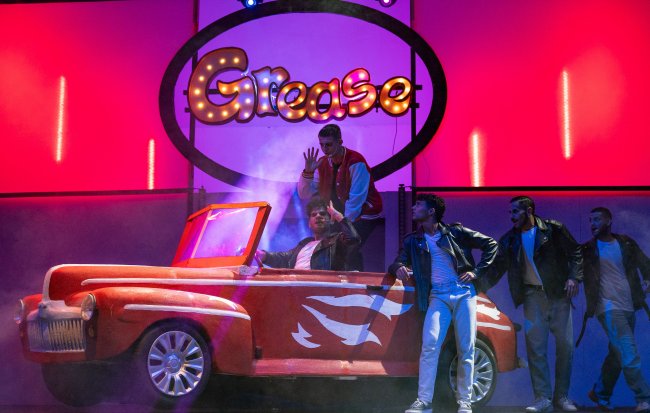 Scena di Grease con ragazzi e un'auto stilizzata.