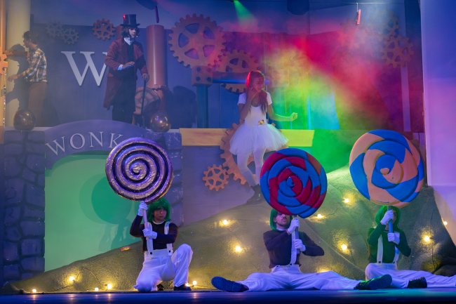 Attori con megadire lollipop e costumi da Oompa-Loompa su un palco colorato.