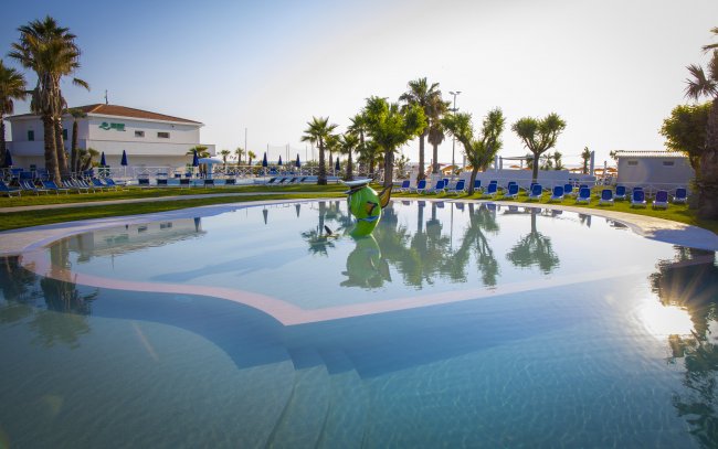 Piscina con decorazione marina e lettini blu, circondata da palme.