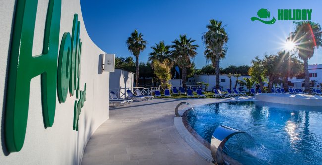 Una piscina con sdraio, palme e la scritta 