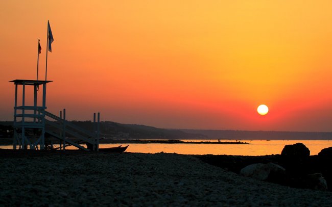Spiaggia al tramonto con una torretta di salvataggio e bandiere.