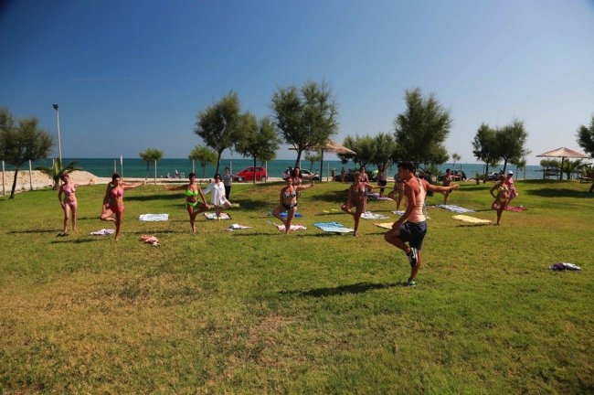 Persone fanno esercizi di yoga su un prato vicino al mare sotto un cielo azzurro.