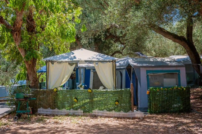 Una tenda da campeggio con gazebo bianco e siepe decorativa con fiori gialli.