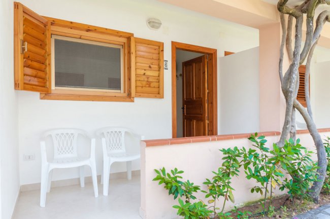 Due sedie bianche davanti a una veranda con finestre e porta in legno, vicino a un giardino.