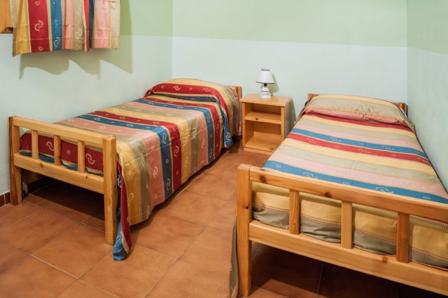 Due letti singoli con copriletti colorati, un comodino e una lampada.