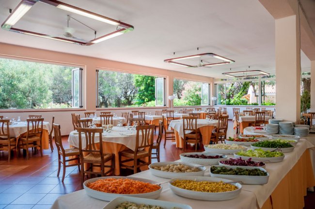 Interno di un ristorante con tavoli apparecchiati e finestre aperte su un giardino.