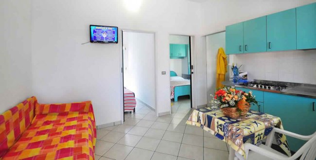 Soggiorno con divano a quadri arancione, cucina blu e tavolo con tovaglia decorata.