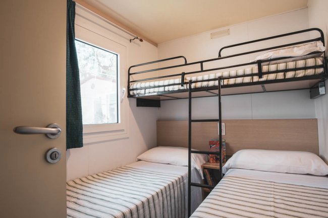 Cameretta con letto a castello e due letti singoli, decorazione semplice e finestra.
