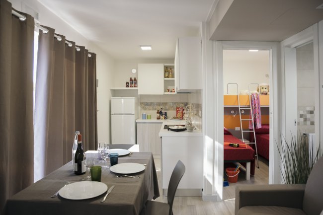 Cucina e sala da pranzo con tavolo apparecchiato, vista su stanza con letti a castello.