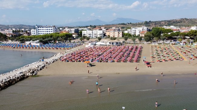 Spiaggia affollata con ombrelloni colorati, mare e edifici sullo sfondo.