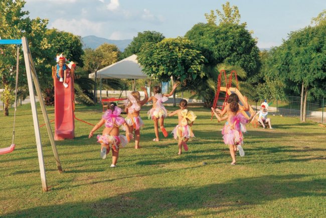 Bambini in costumi colorati giocano in un parco con scivoli e altalene.