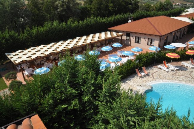 Piscina con ombrelloni, vegetazione intorno.
